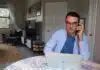 man in white dress shirt wearing eyeglasses sitting by the table using macbook