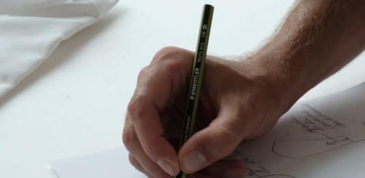 person holding black pencil on white printer paper